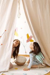 Cute little girls with angel wings costume sitting on mat and playing with paper birds