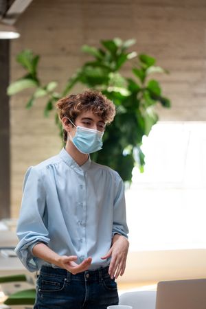 Nonbinary person wearing a face mask and standing talking with colleagues in a bright modern office