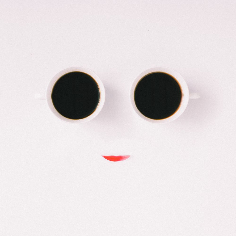 Face made of two coffee cups and pink flower petal on light background