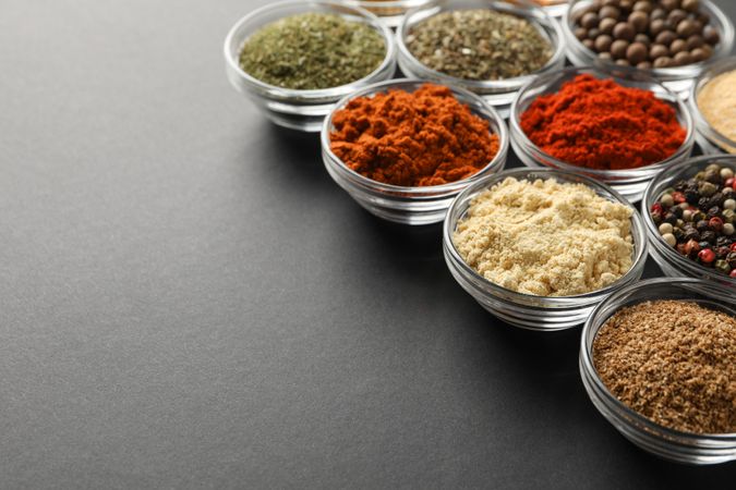 Glass bowls full of spices arranged diagonally on dark table with copy space