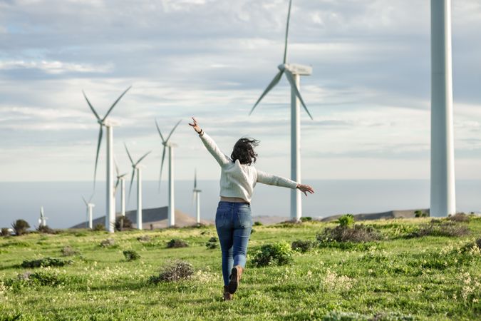 Excited woman running on green grass nearby wind turbine farm in Lanzarote, Spain
