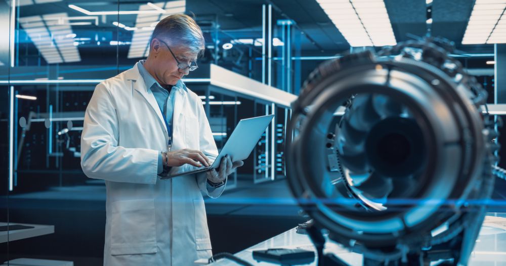 Adult Chief Engineer Using Laptop Computer, Analyzing and Researching How a Futuristic Turbofan Motor Works.