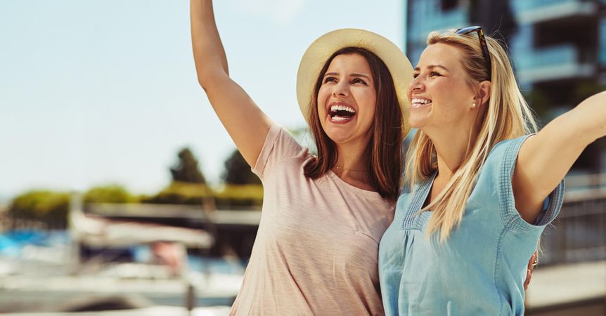 Women smiling and standing together with their arms up on sunny day, copy space