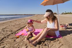 a girl putting sunscreen cream on her mother at the beach