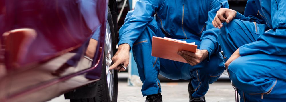 Two male mechanics crouched down looking at vehicle tire
