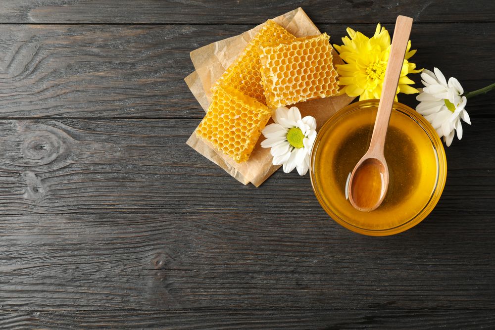 Bowl with honey, honeycombs and flowers on wooden background, copy space
