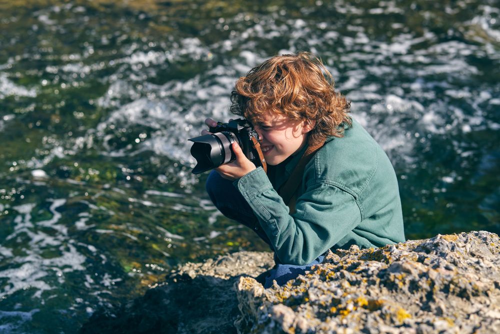 Positive boy taking photo near flowing water