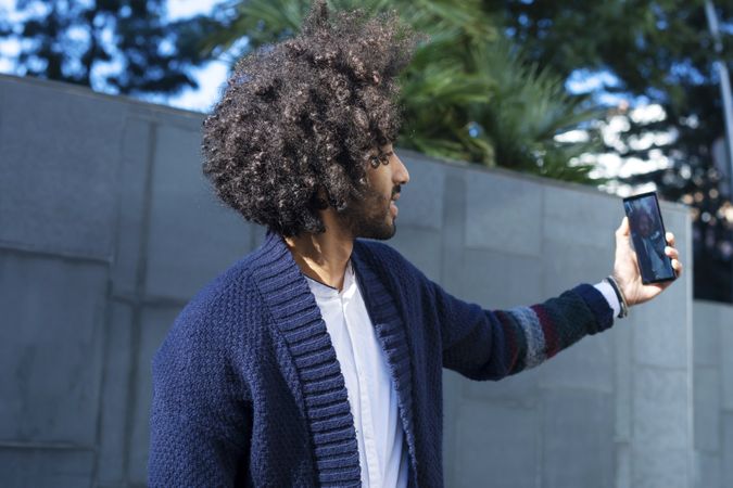 Black man in cardigan taking selfie outdoors in the sun