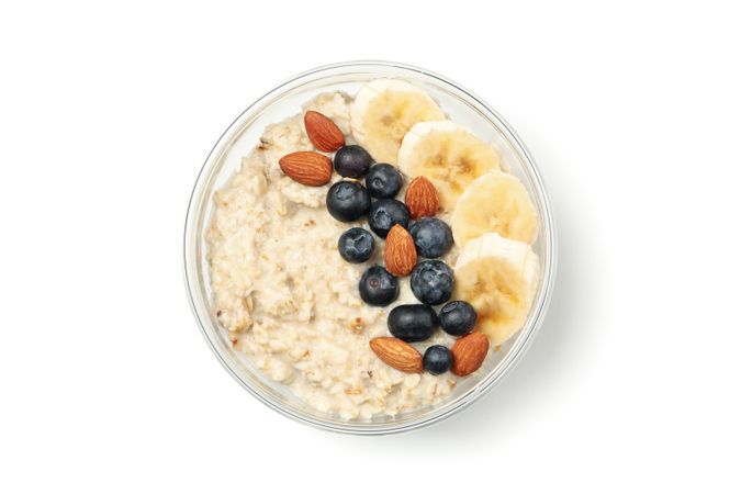 Bowl with oatmeal porridge and ingredients isolated on plain background