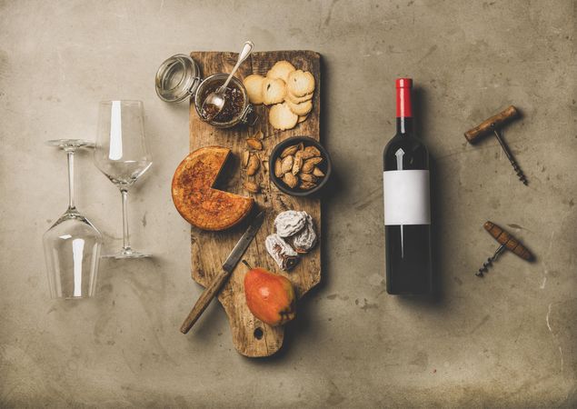 Cheese plate with red bottle of wine, two glasses, and corkscrews