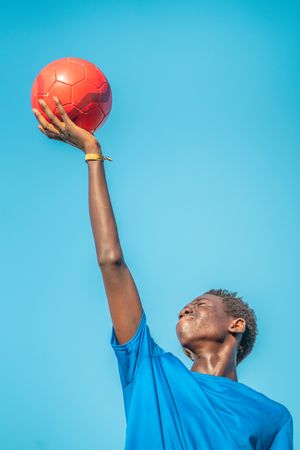 Black teenager with football ball against sky