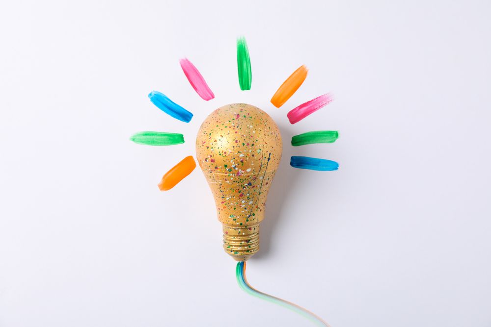 Light bulb with paint splatters on light background, space for text
