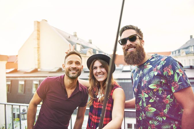 Friends smiling on rooftop while holding a selfie stick above them