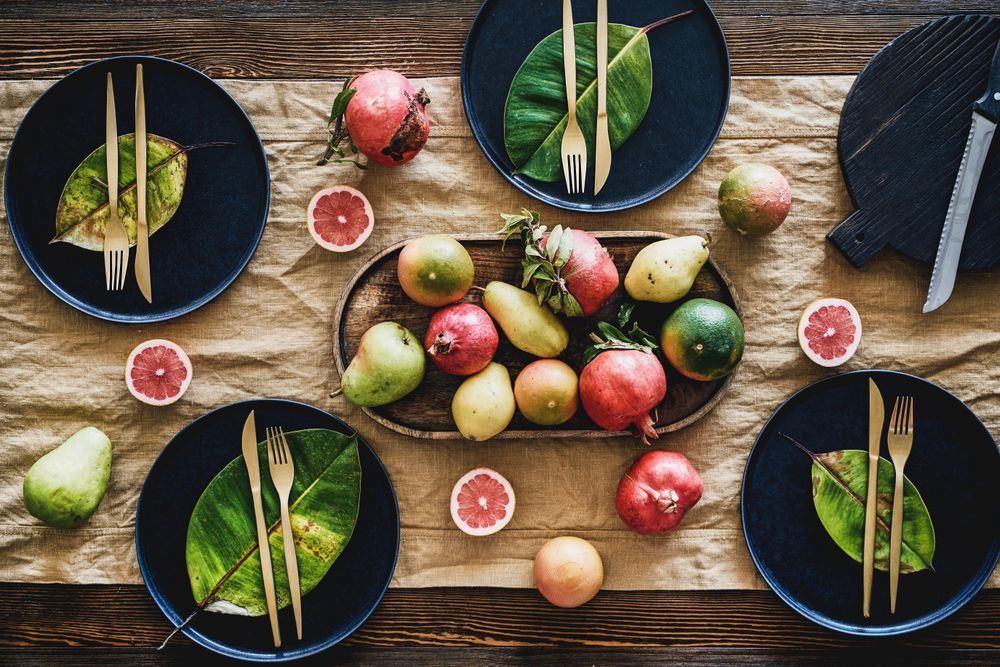 Fresh table setting with leaves on dark plates, with fruit