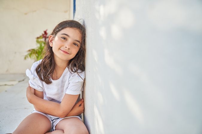 Charming girl sitting on street near wall
