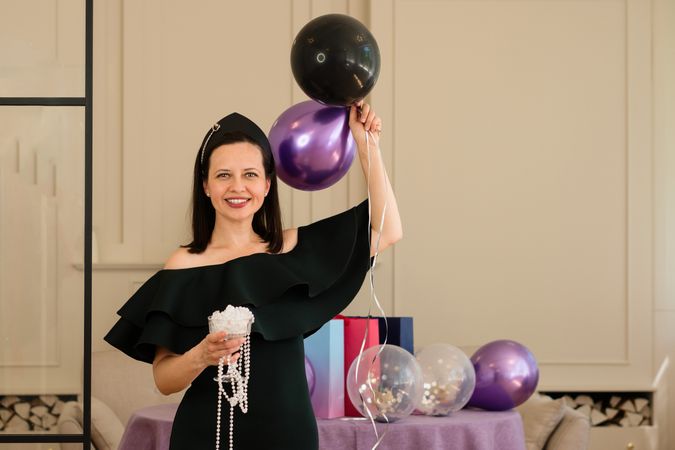 Woman holding balloons, smiling at birthday party.