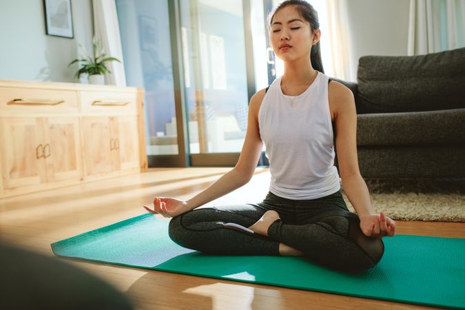 Healthy young woman meditating in lotus pose at home
