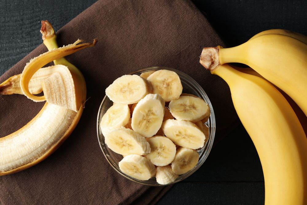 Bowl of banana slices, banana and towel on wooden background