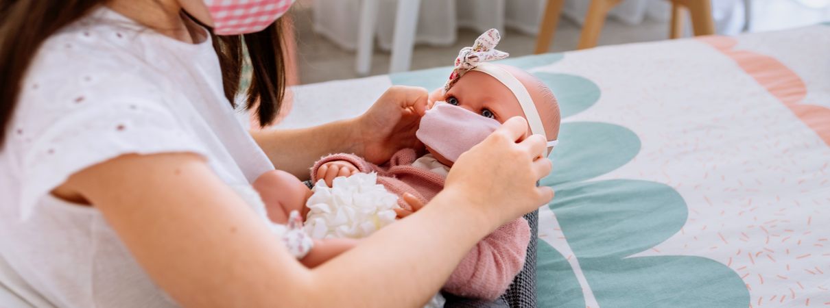 Girl with mask putting small mask on her doll