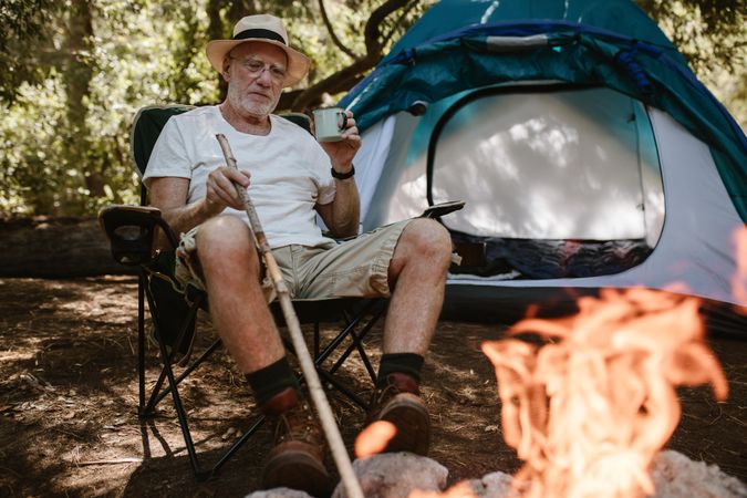 Mature man sitting relaxed near campfire and with a cup of coffee