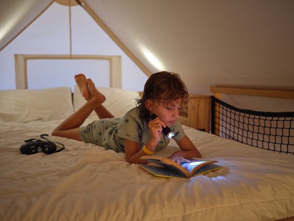 Boy reading with flashlight on bed