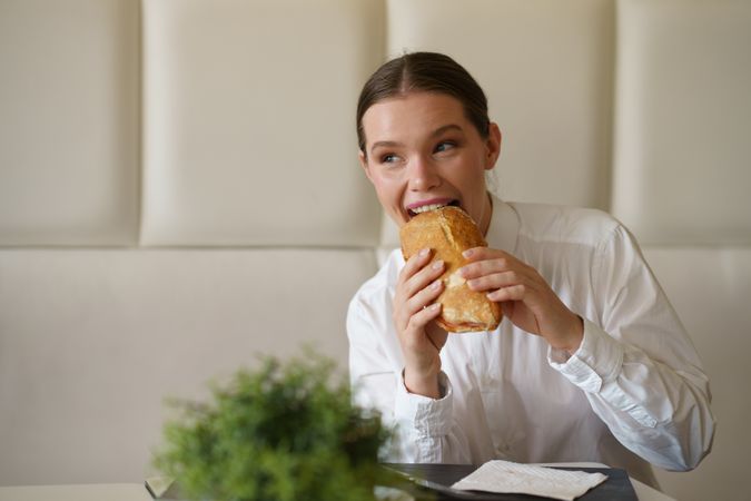 Cute businesswoman biting a sandwich in a modern cafeteria
