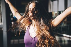Young brunette with long waving hair moving while dancing in sunlight.