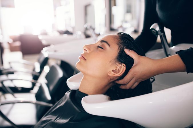 Young woman resting head in hands of hairdresser over salon sink