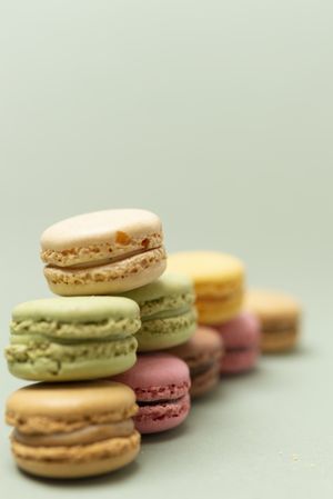 Pile of sweet pastel macaroons over a green background, vertical with copy space