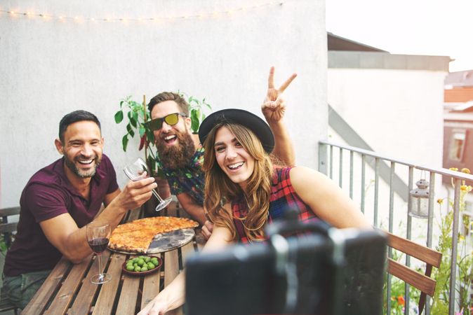 Group of friends smiling with pizza and wine while taking a photo with a selfie stick