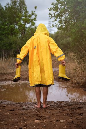 Barefoot kid with gumboots standing near puddle