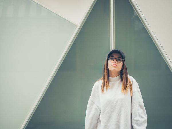 Young woman with glasses standing against wall