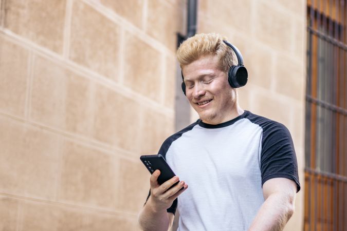 Albino manLatino man with albinism down the street using smartphone and listening to music with headphones