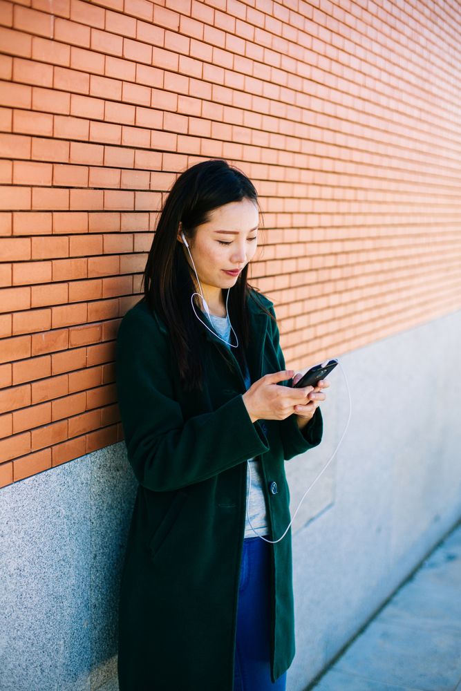 Asian female listening to music near brick wall
