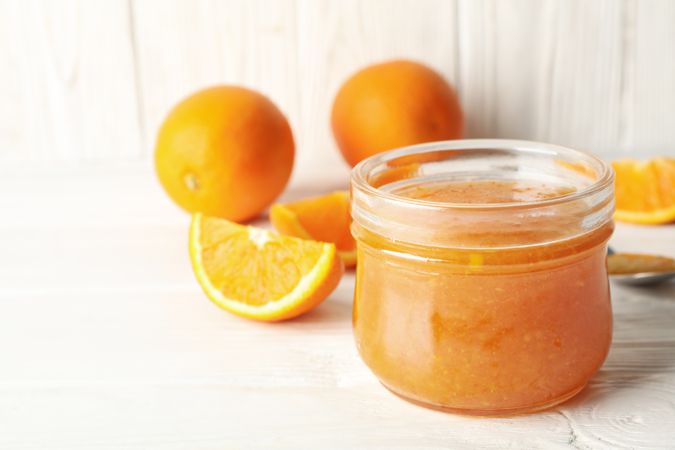 Oranges, spoon and glass jar with jam on wooden background