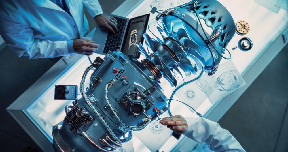 Top Down View of Two Engineers Discussing Work, Talking, Using Laptop Computer and Checking Blueprints in Jet Motor Manufacturing Facility.