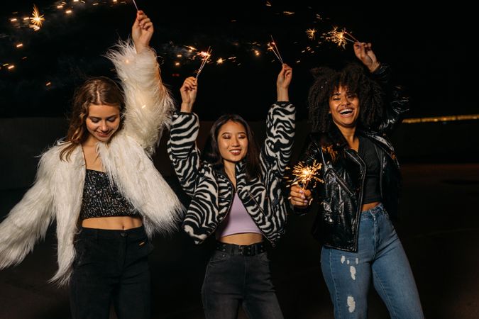 Three women celebrating at night with sparklers with their arms up