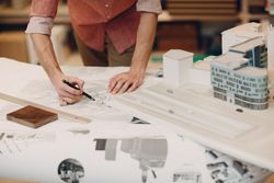 Cropped image of an architect drawing on a blueprint beside building models
