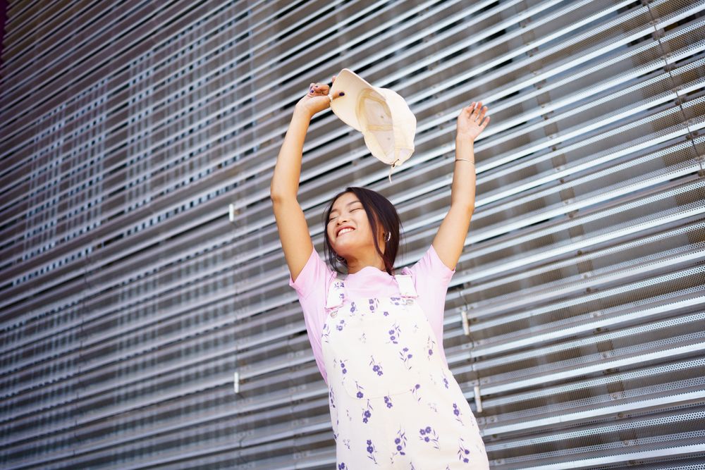 Smiling female in floral overalls with hands and cap above her head