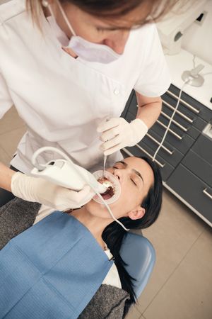 Female doctor examining teeth of patient with 3D scanner