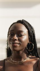 Portrait of a young Black woman, with braids in her hair, enjoying a summer afternoon in front of her house