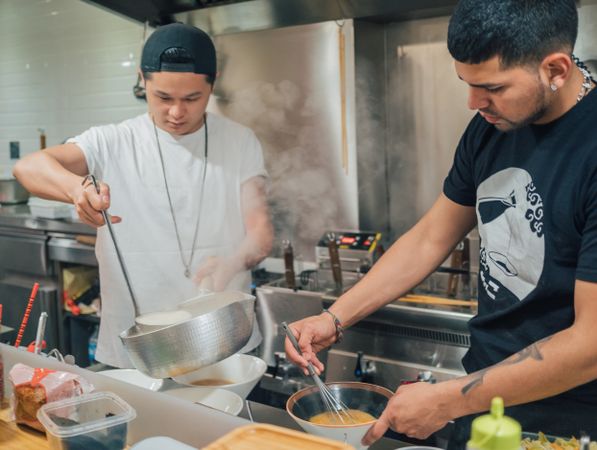 Asian males pouring soup in kitchen