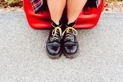 Woman sitting on red suitcase on road