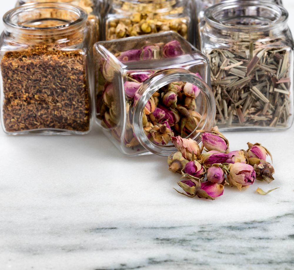 Spices and herbs in small glass jars pouring onto marble stone background