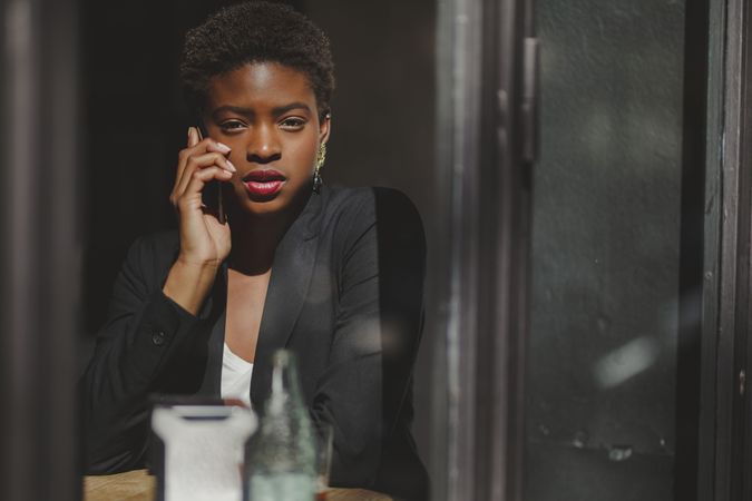 Serious stylish Black woman talking on smartphone in cafe
