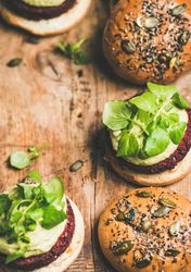 Close up, vegan burgers on seeded buns arranged on wooden board, vertical composition, copy space