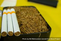 Close up of cigarettes resting on box of loose leaf tobacco on yellow table 0LdLGy