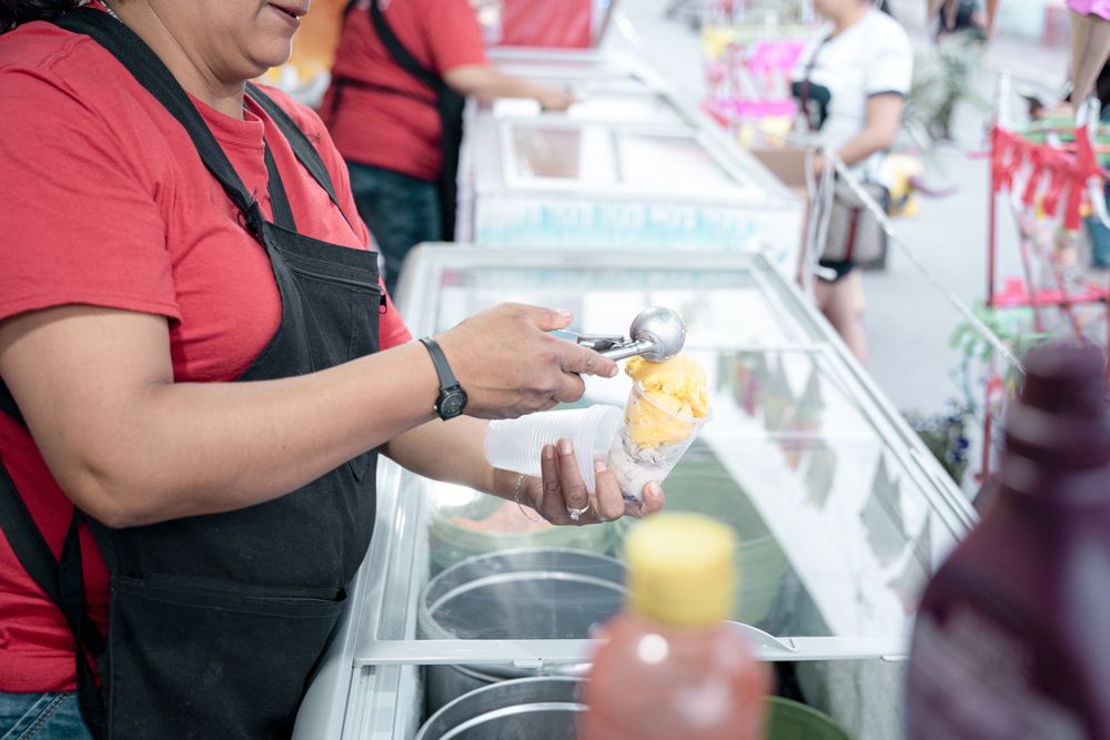 An Hispanic adult woman is serving some vanilla ice cream balls in a cup in the street