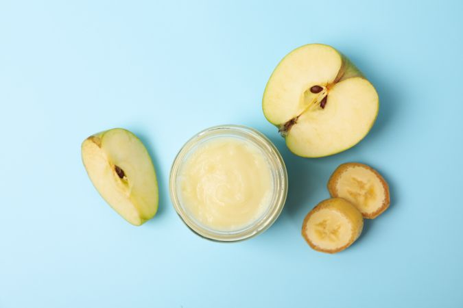 Glass jar with apple puree on blue background, top view