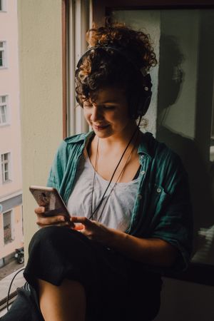 Cheerful woman in headphones using smartphone at home